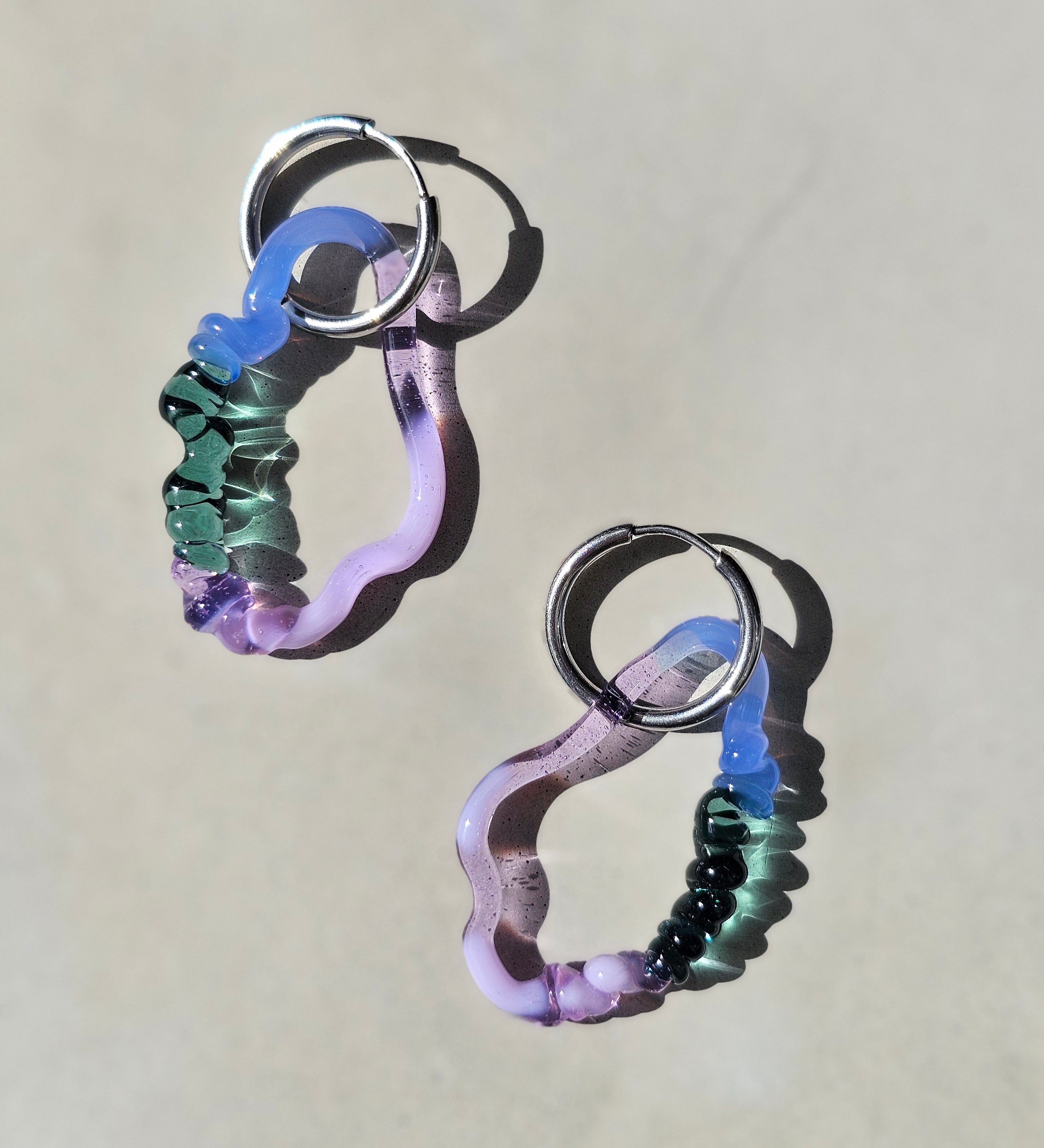 KLAPPERGLAS Drift Hoops candy deep tide mit wellenförmigen Glasanhängern in Flieder, Blau und Petrol an silberfarbenen Creolen kitsch kiosk